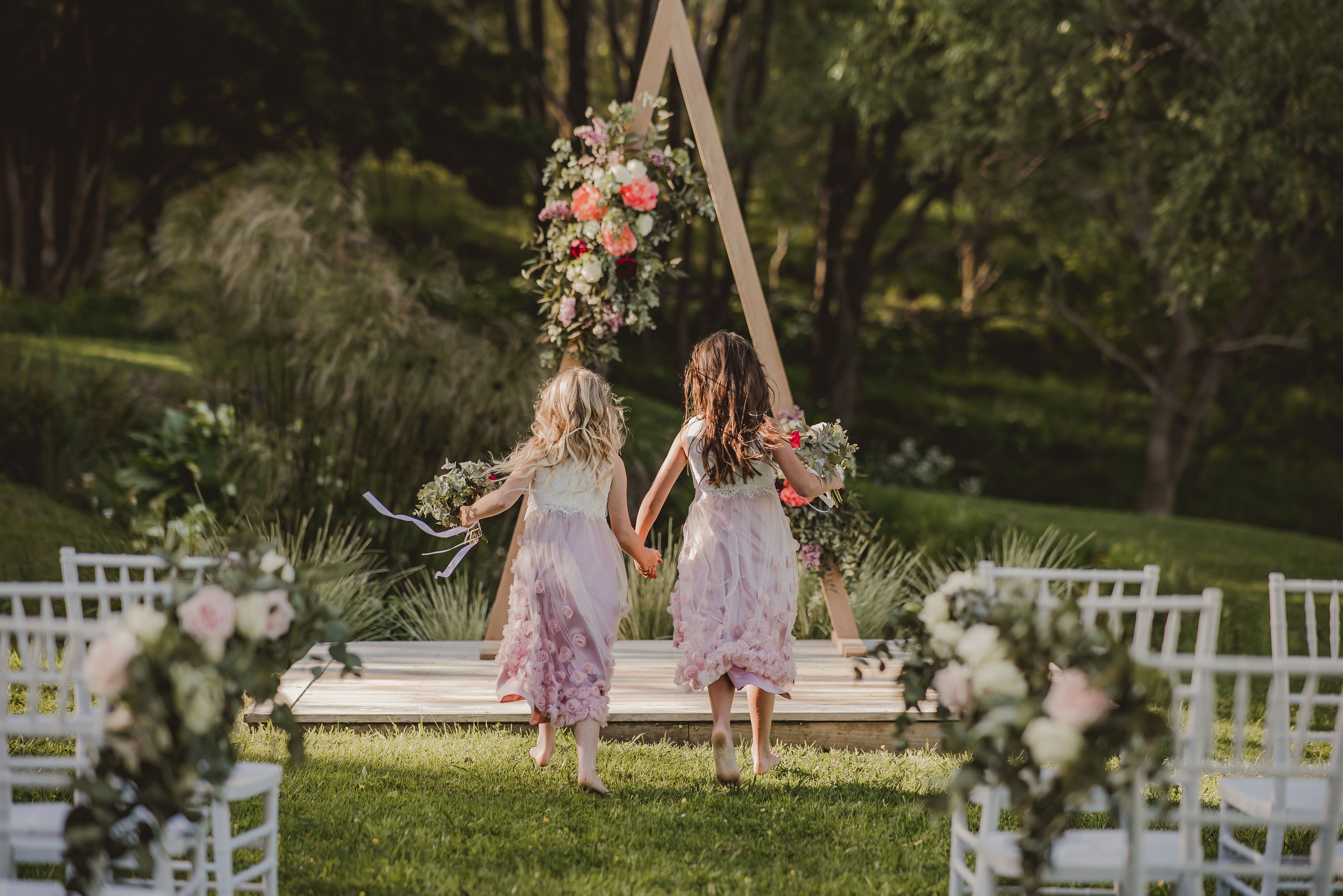Flower girls running towards wedding arch with fresh flowers peonies