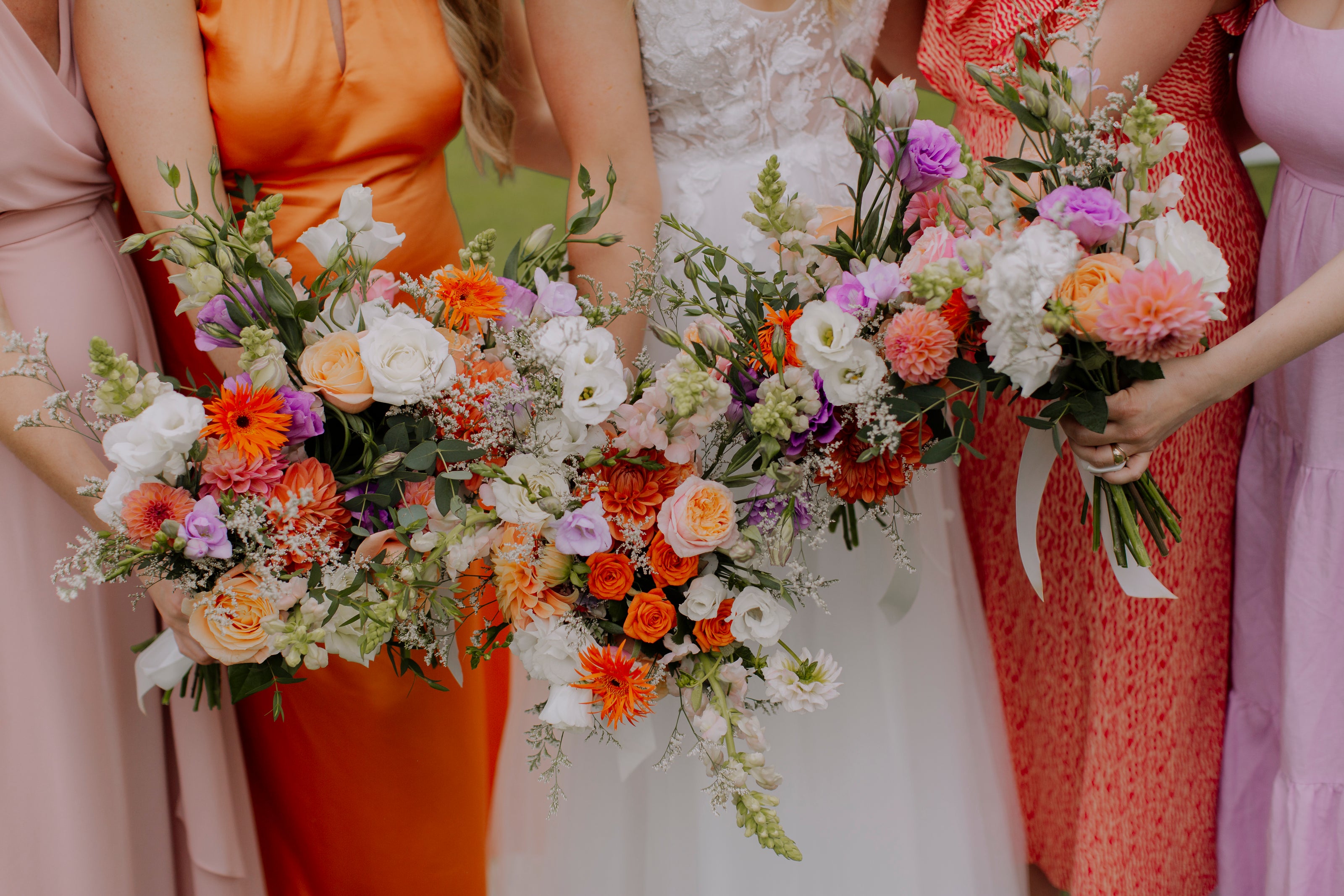 Close up of orange, purple and white bridal party fresh flower bouquets