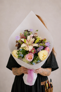 Person holding a bouquet of flowers wrapped in white paper against a plain background