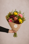 Bouquet of flowers wrapped in brown paper held by a person against a plain background