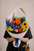 Person holding a colorful bouquet of flowers wrapped in white paper against a neutral background