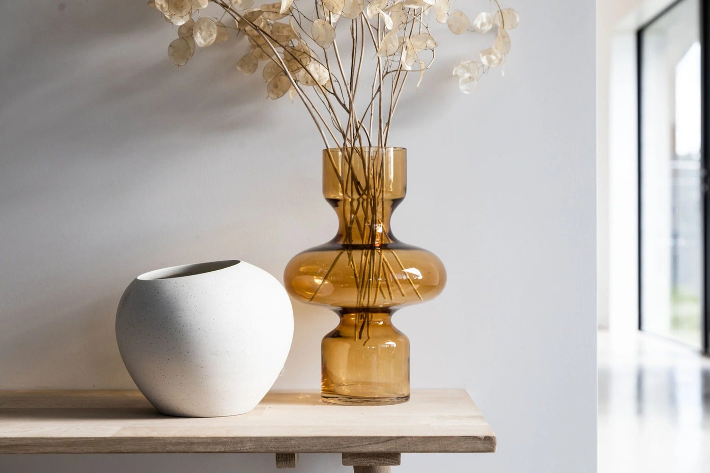 Two vases, one white ceramic the other yellow glass with dried flowers